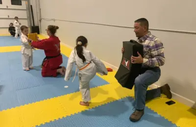 Martial arts student kicking training pad held by parent