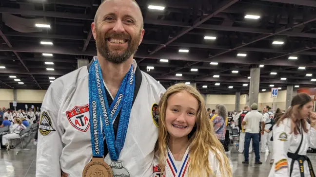 Instructor posing with a student wearing a medal after martial arts event